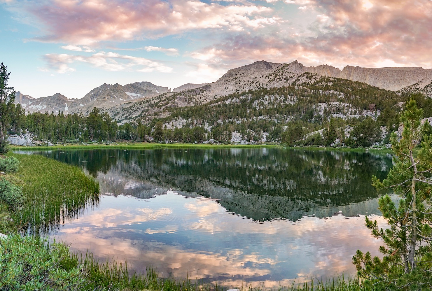 A sunset sky reflects in an alpine lake surrounded by pine trees and mountains in Sequoia and Kings Canyon National Park