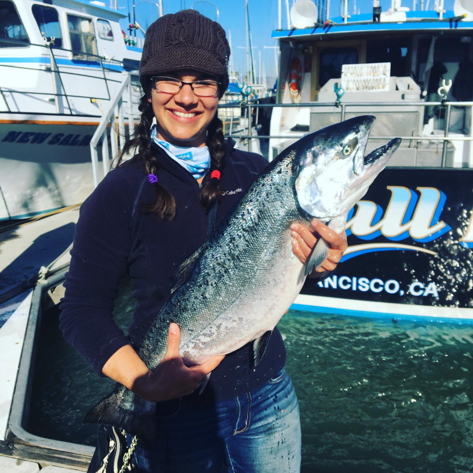 Woman scientists holds large salmon with boats in the background