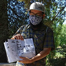 Man wearing face covering holds sketch book.