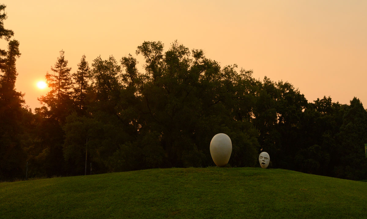 Two Egghead sculptures under hazy colored sky.
