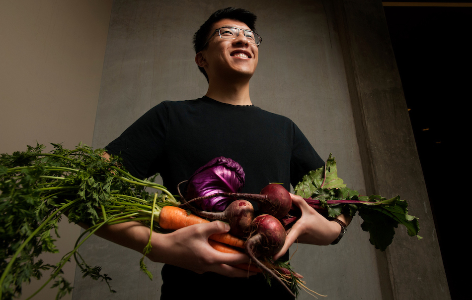 Student smiles while holding a bundle of bright vegetables. 