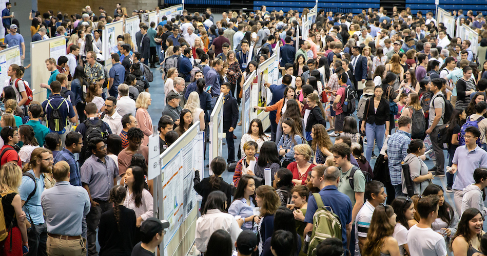 A large amount of students visit booths in a crowded pavilion.
