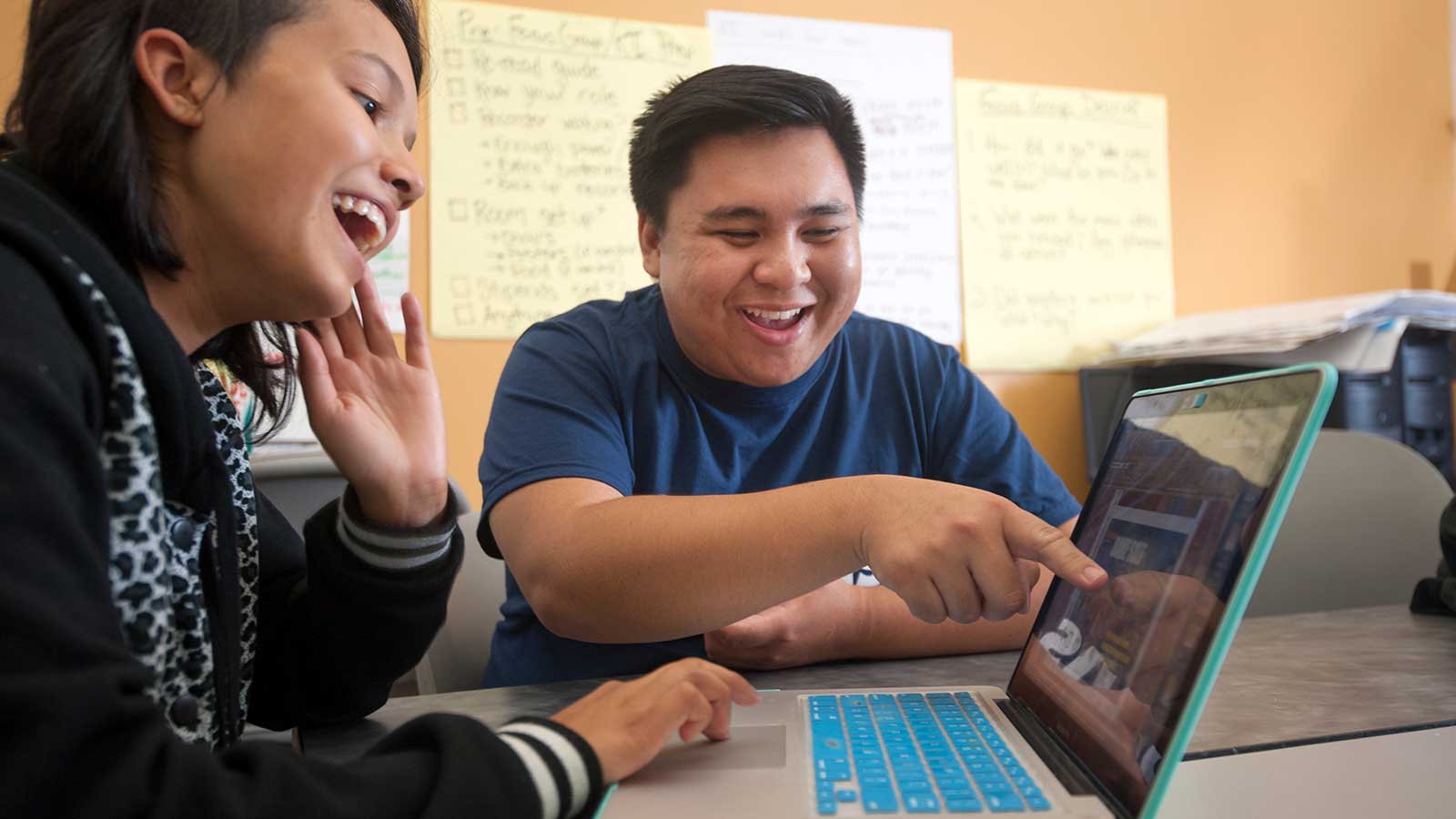 Young woman and man laughing as he points to a computer screen