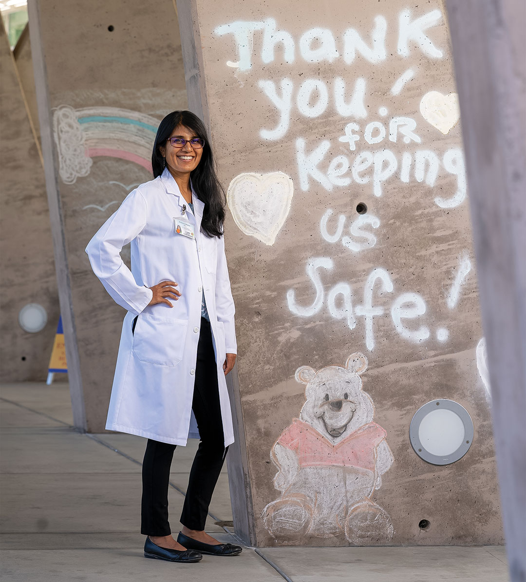 A woman doctor stands by graffiti that says 'thank you for keeping us safe'