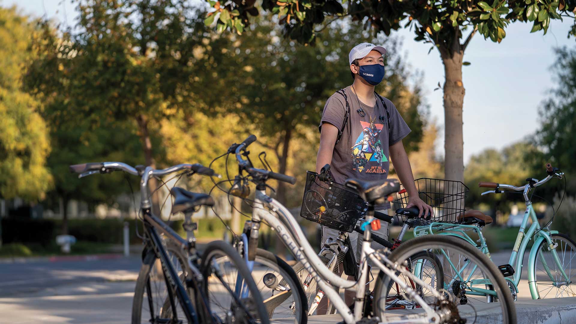 A student stands with bikes on campus and wearing a face mask