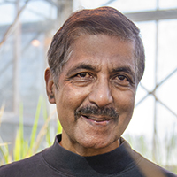 Face of a smiling man with brown skin, dark hair and a mustache. 