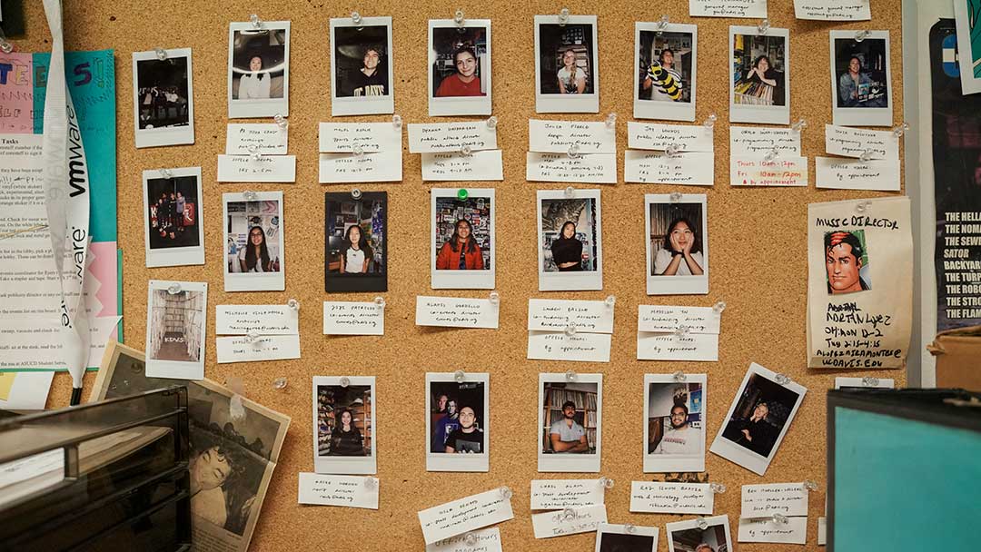 Photo of a bulletin board with a grid-like arrangement of polaroid headshots and small pieces of paper with handwritten names and titles under each photo.