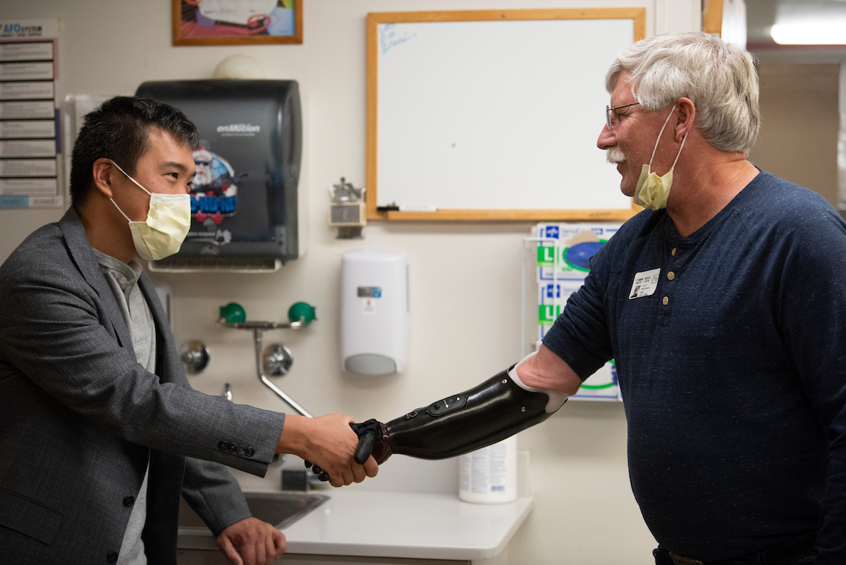 Surgeon Andrew Li shakes the prosthetic hand of former patient David Brockman, a retired fire captain, who had targeted muscle re-innervation surgery on his amputated hand. (Greg Urquiaga/UC Davis)