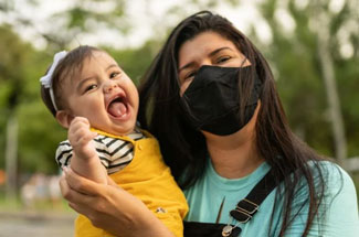 Woman in face mask holds smiling infant
