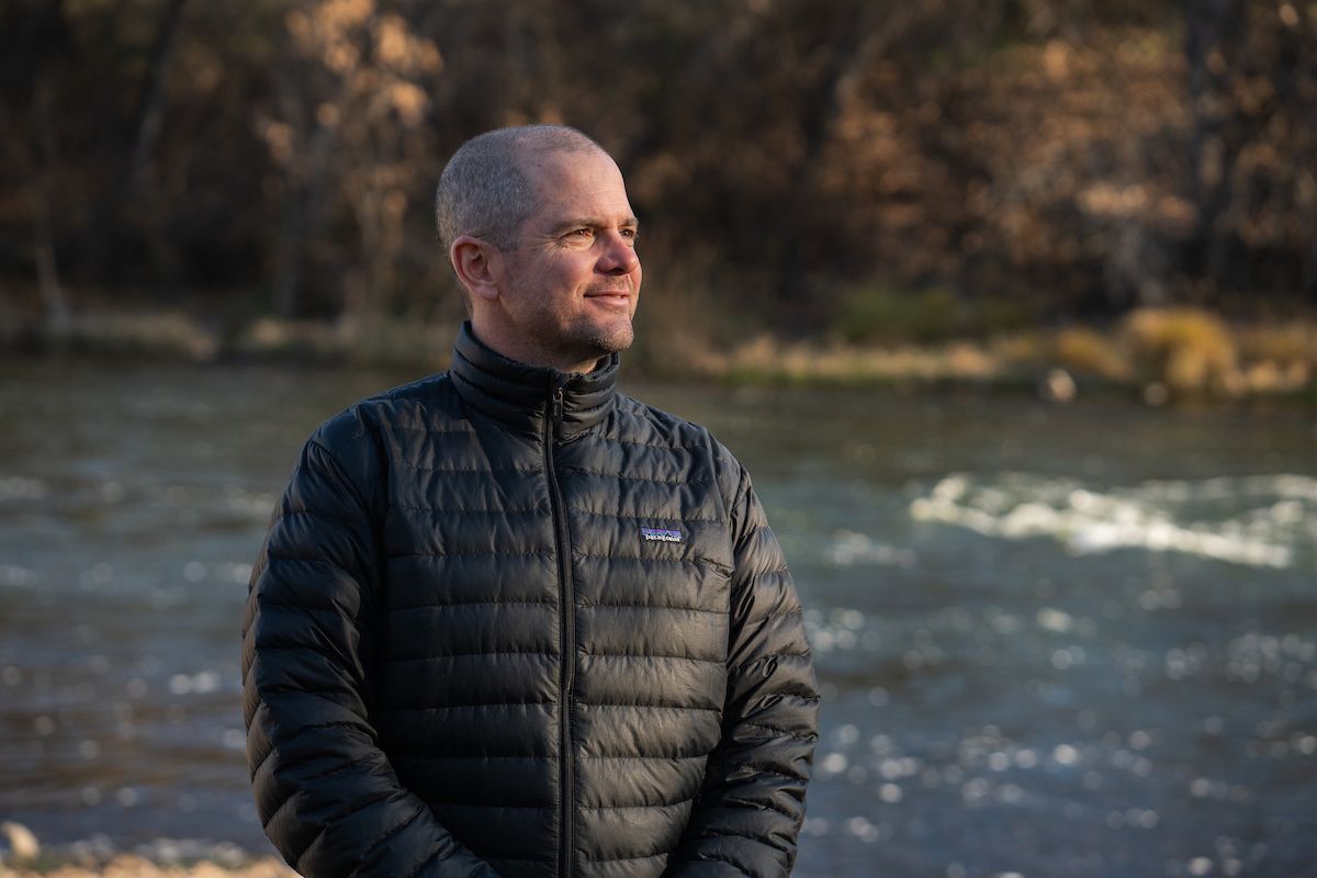 Fish biologist Robert Lusardi stands with hands in pockets showing side profile with Klamath River running in background during winter