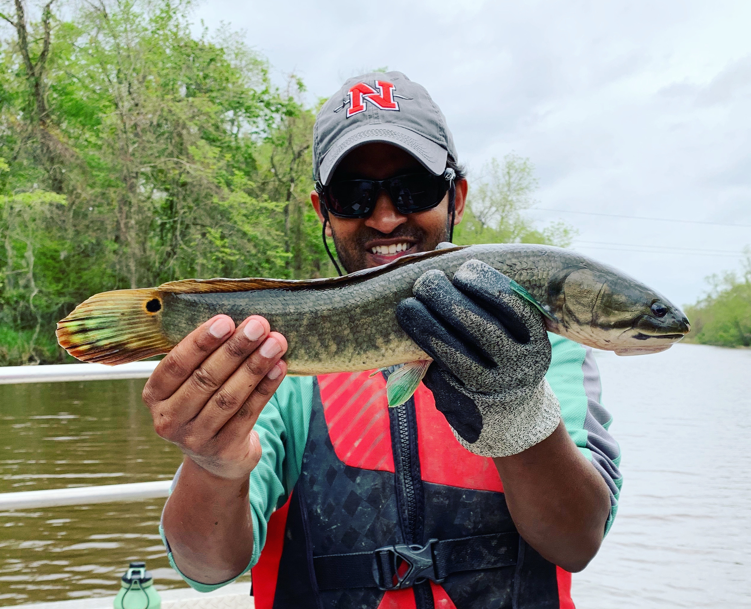 Man with hat smiles holding a medium-sized bowfin fish. It has bright green fins