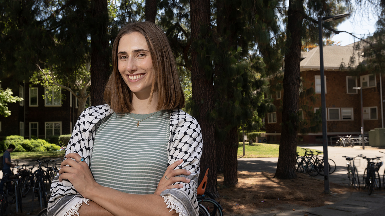 Brooke Morey wears a keffiyeh against a background of trees.