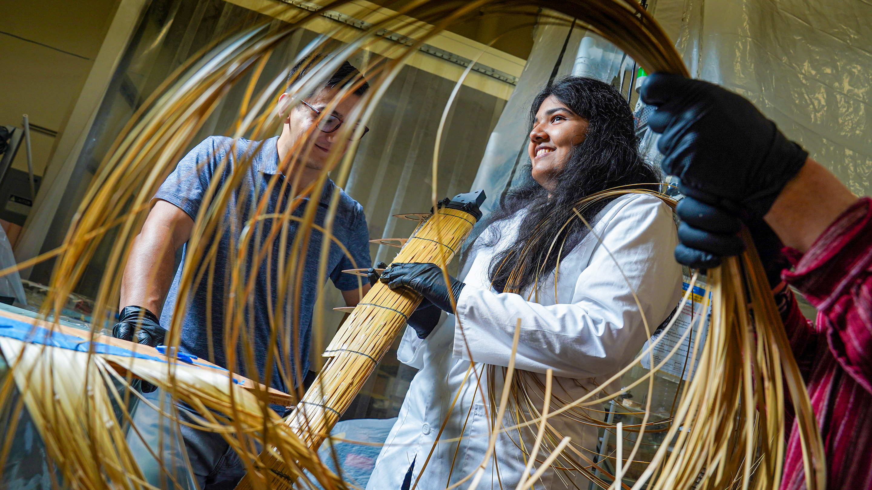 Two students are framed by bamboo as they work on compostable wind turbine blades