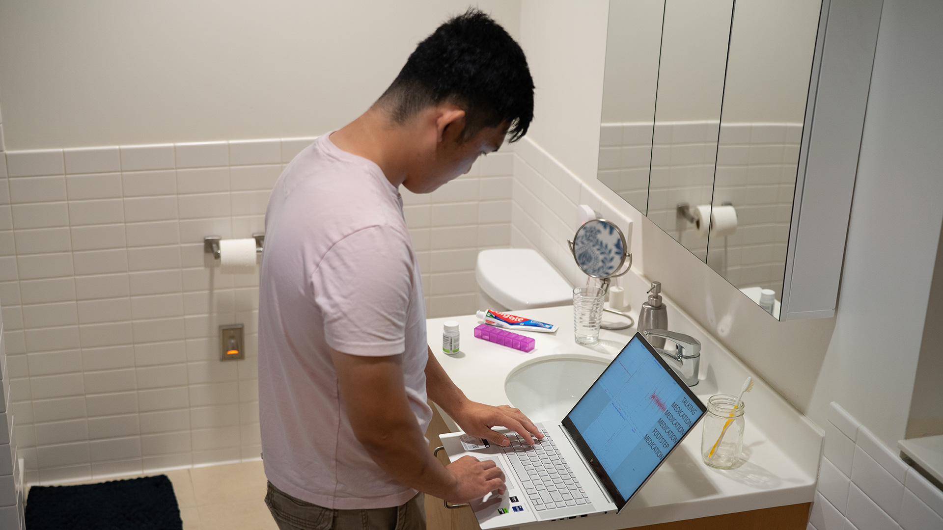 A man works on a laptop in a bathroom