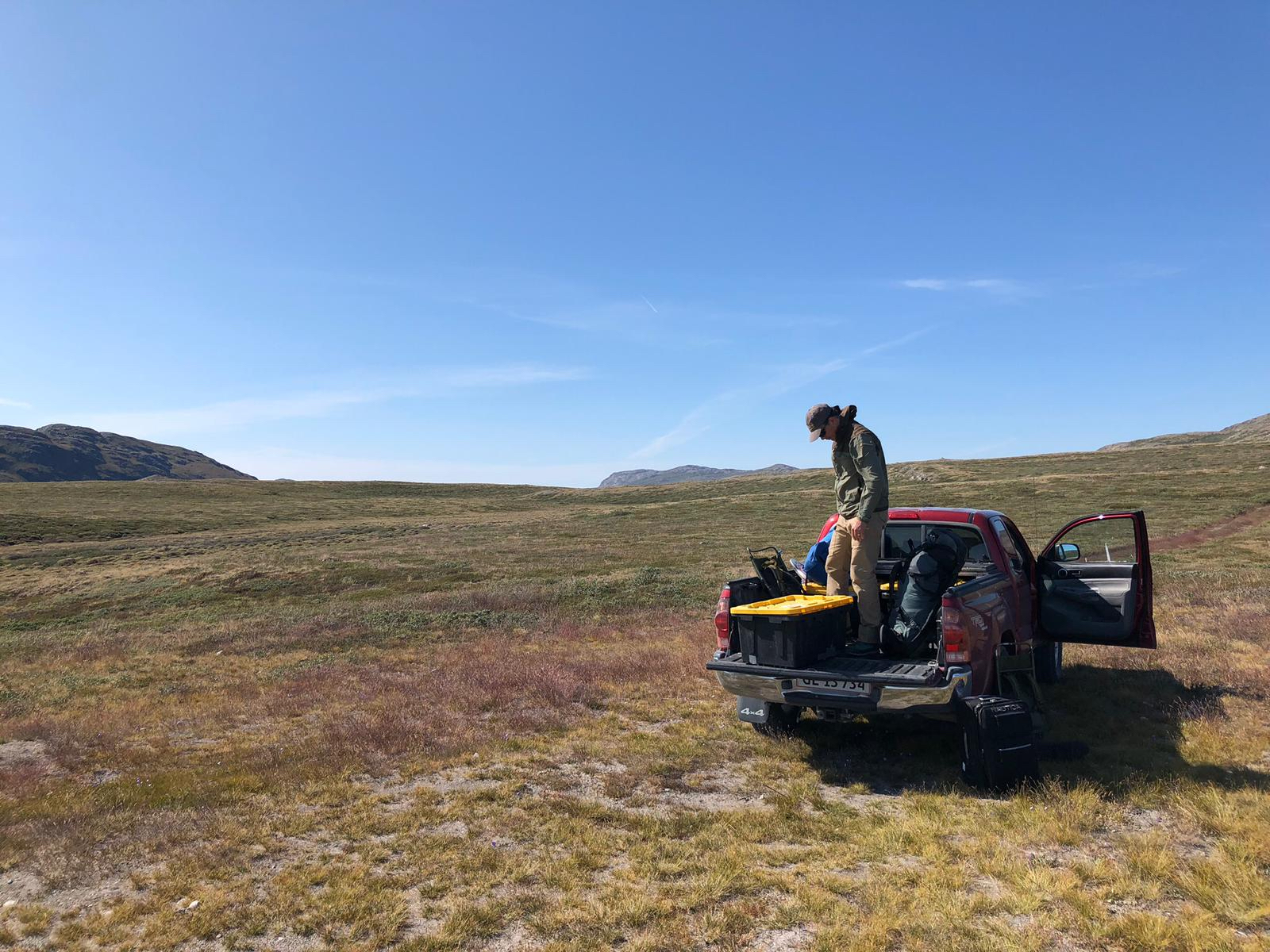 Man stands in back of pickup truck on plains of Greenland