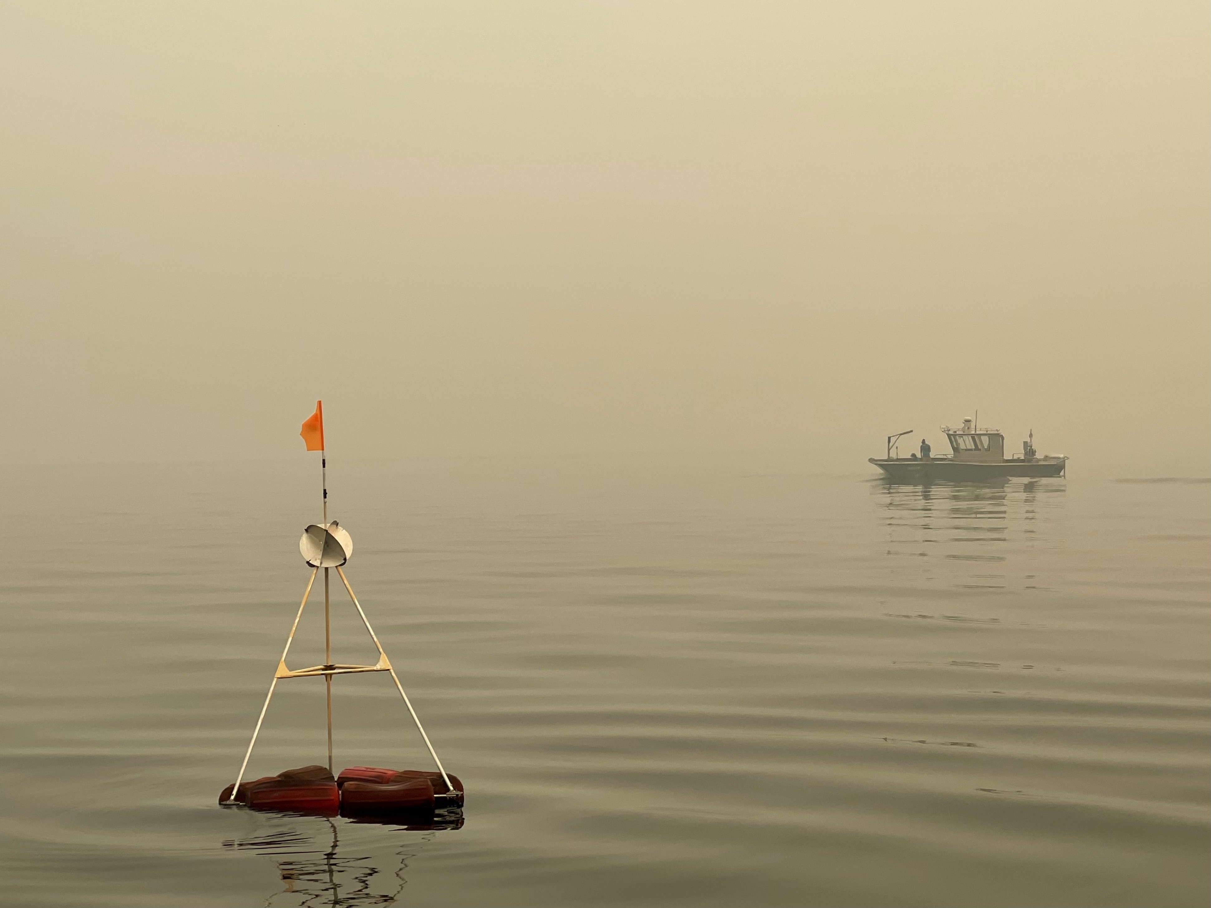 buoy on lake tahoe with research vessel in the background amid smoke-covered skies