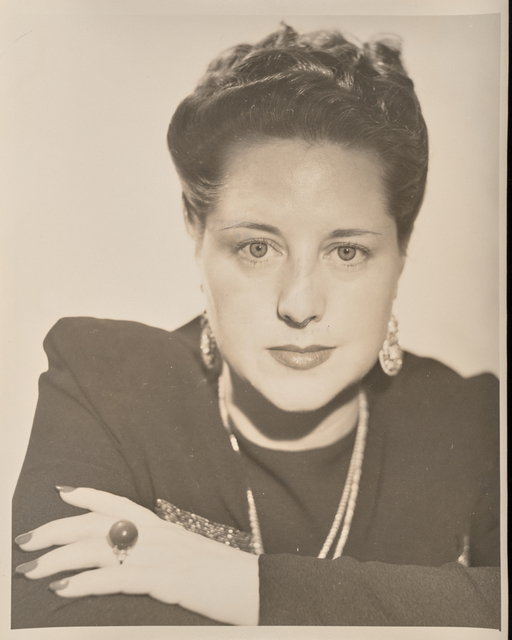 Black-and-white photo of woman, wearing pearls or beads and dark dress or top