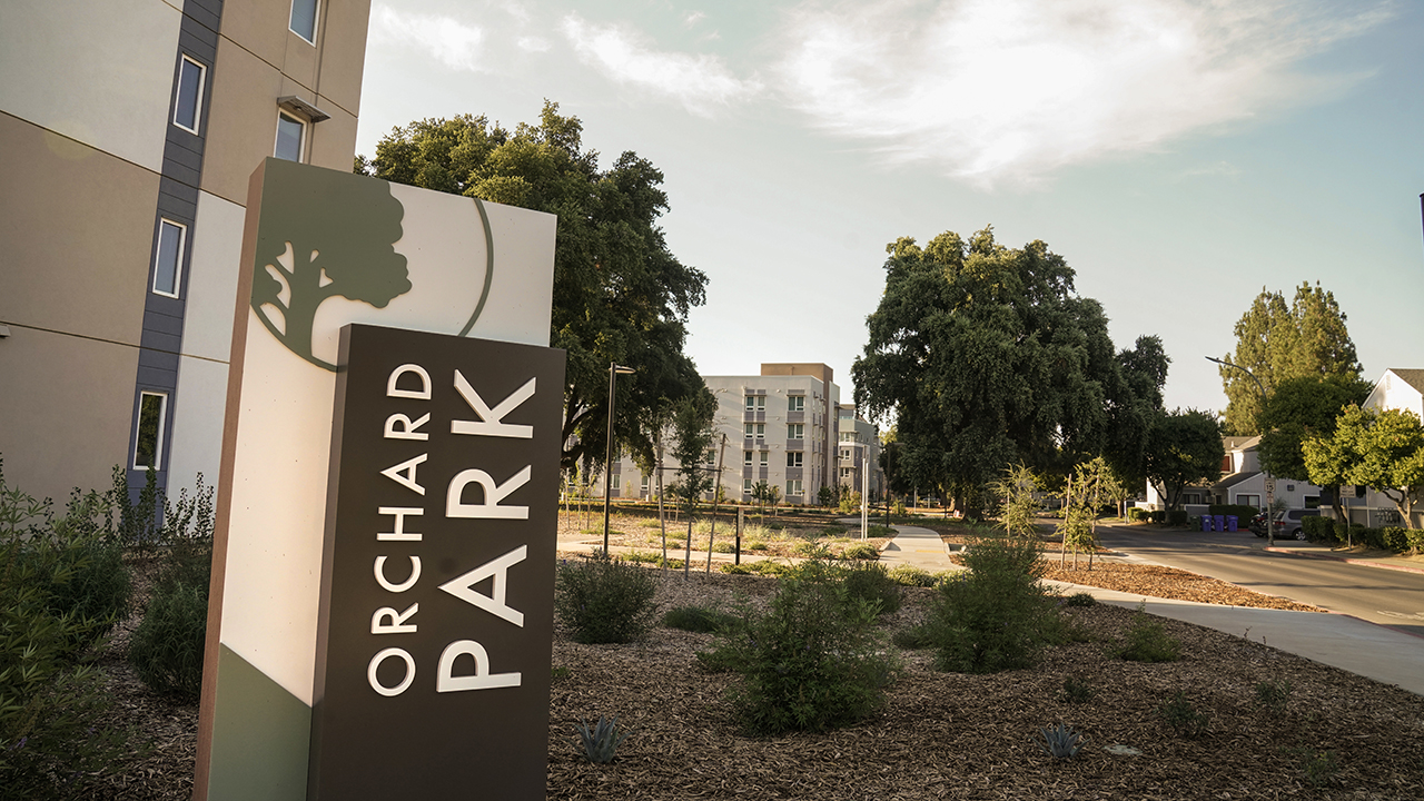 An Orchard Park sign beside an apartment building showing landscape and paths in the background