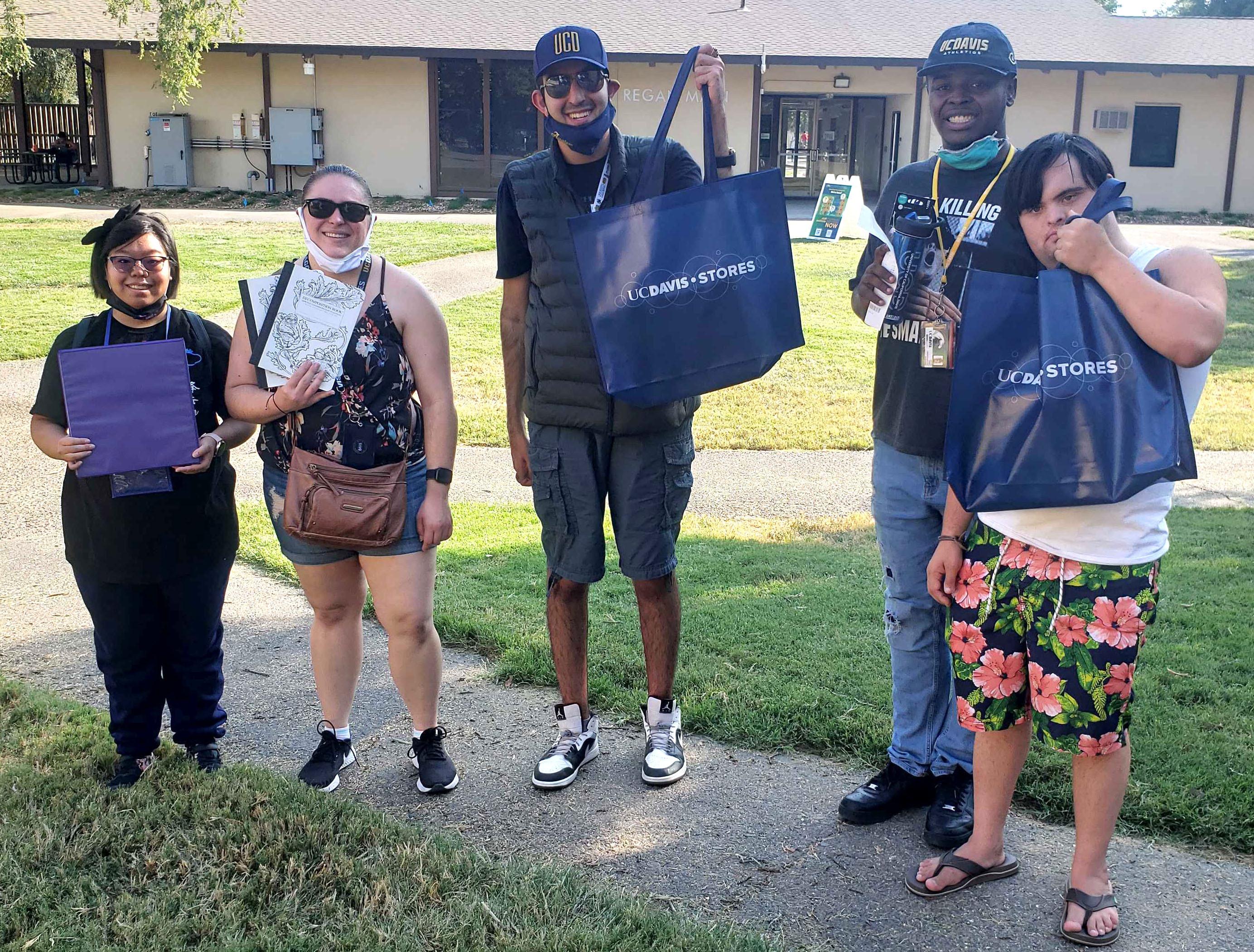 Five students stand on a sidewalk holding UC Davis bags