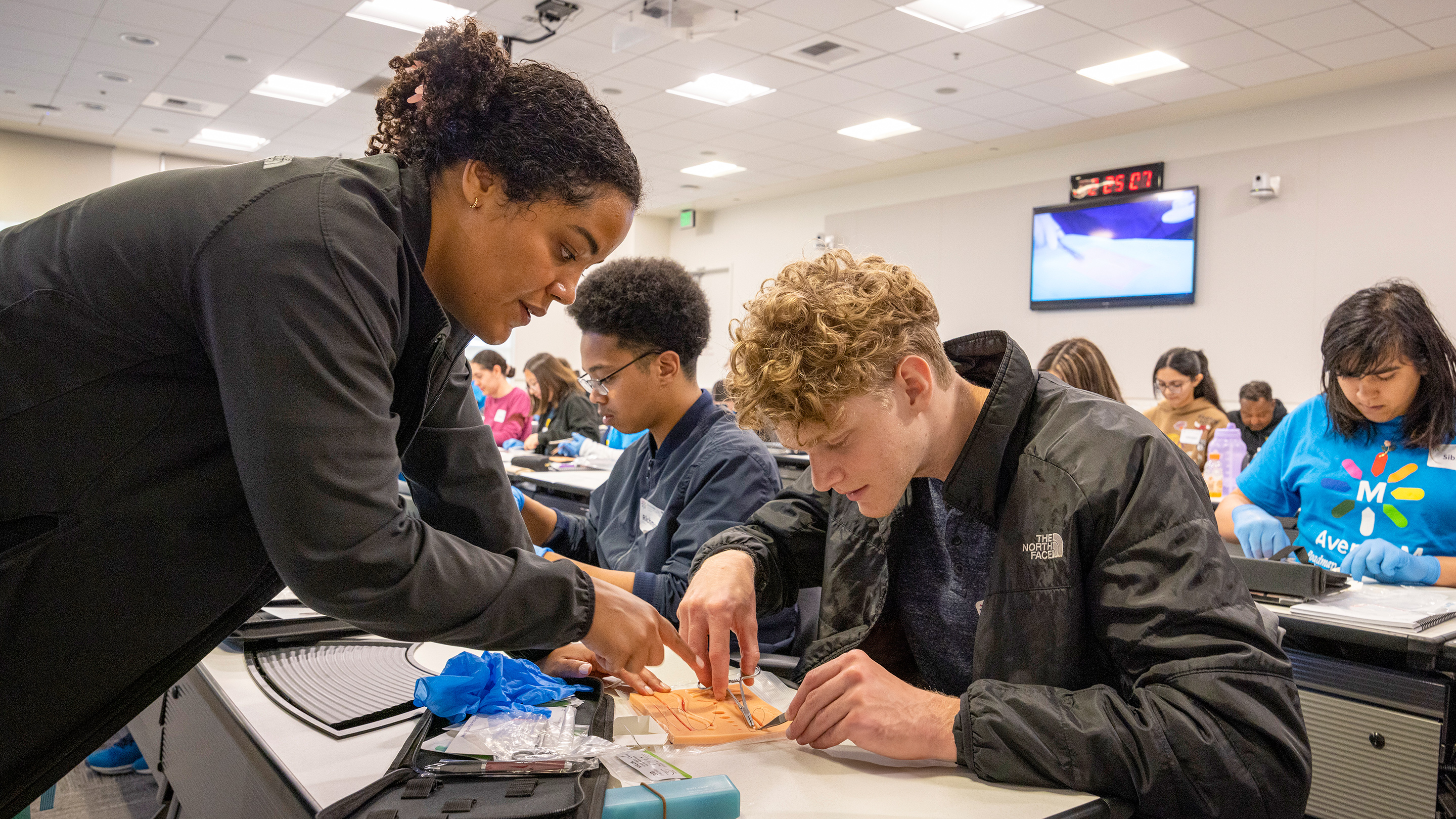 A student works with scissors and a plastic thread under the supervision of an instructor