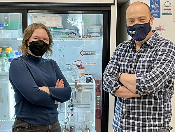 Female and male scientist, facing camera, arms folded, wearing masks