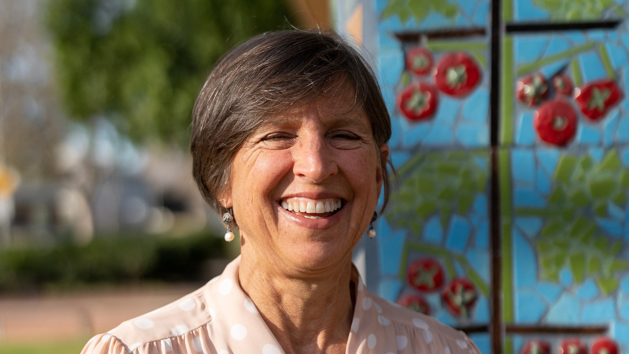Pam Ronald, environmental, posing in front of vegetable-art mosaic column