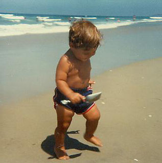 Toddler on a beach with a fish in hand