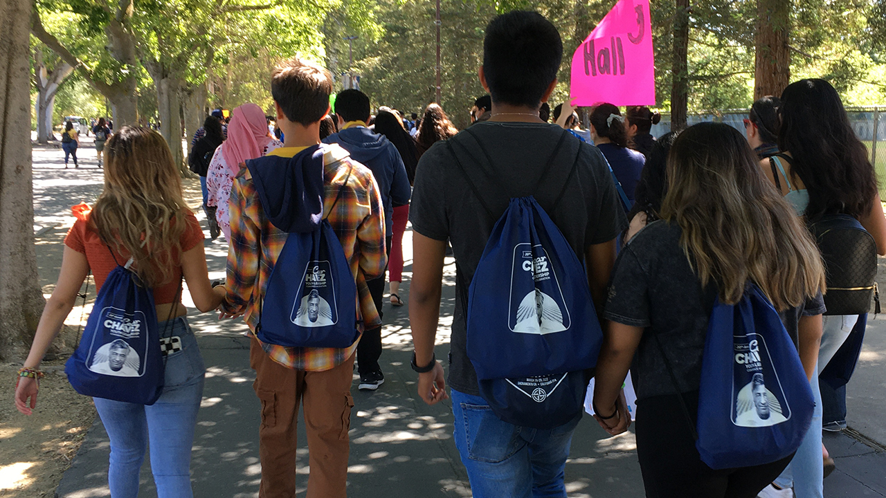 Four students, all wearing Cesar Chavez conference backpacks follow other students to a workshop