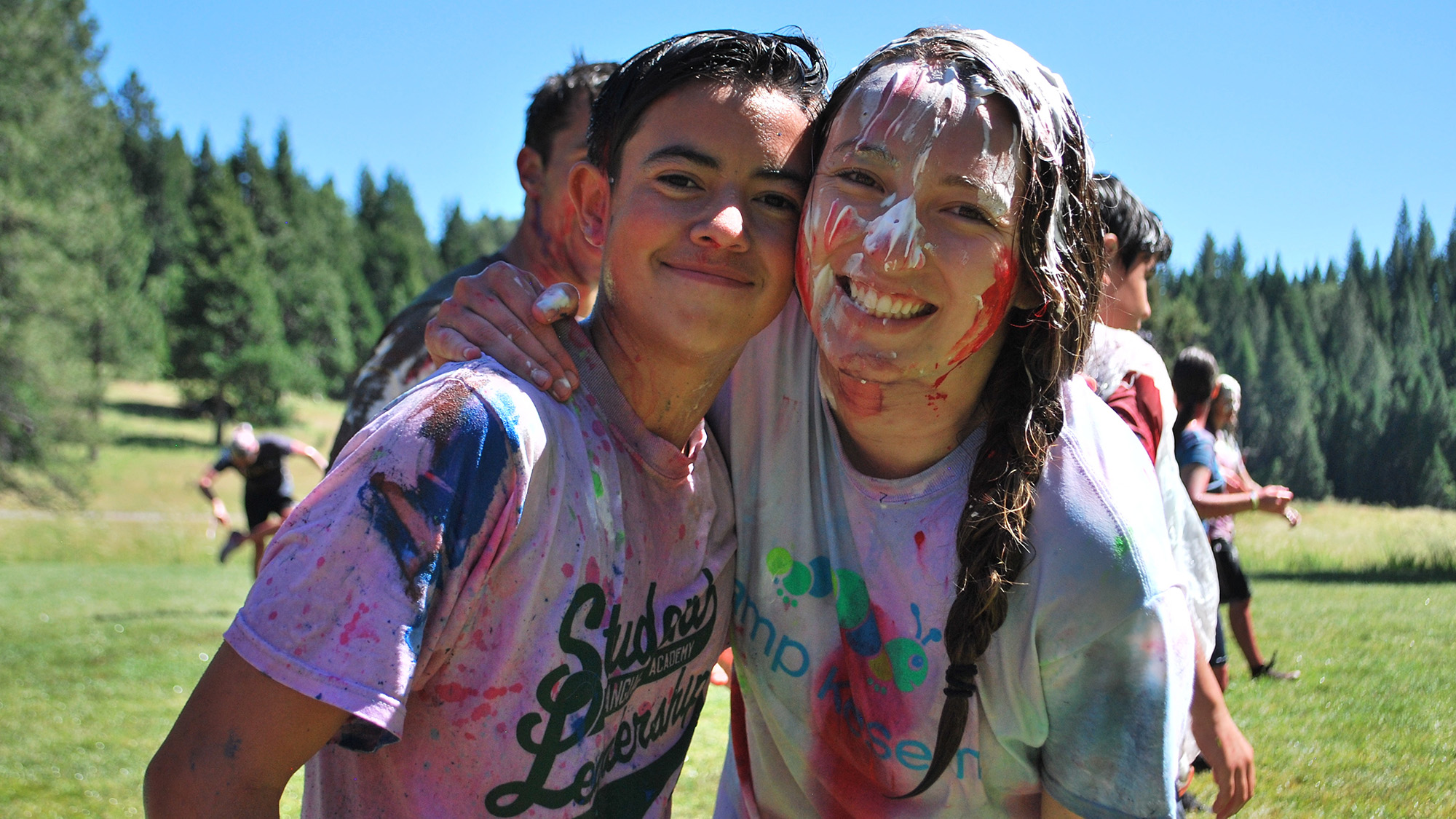 Camp counselor with paint on her face and clothes embraces a camper.