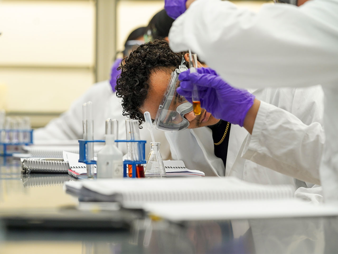 Student in lab coat and safety goggles carefully examining a test tube in a chemistry lab at the Science Laboratory Building.