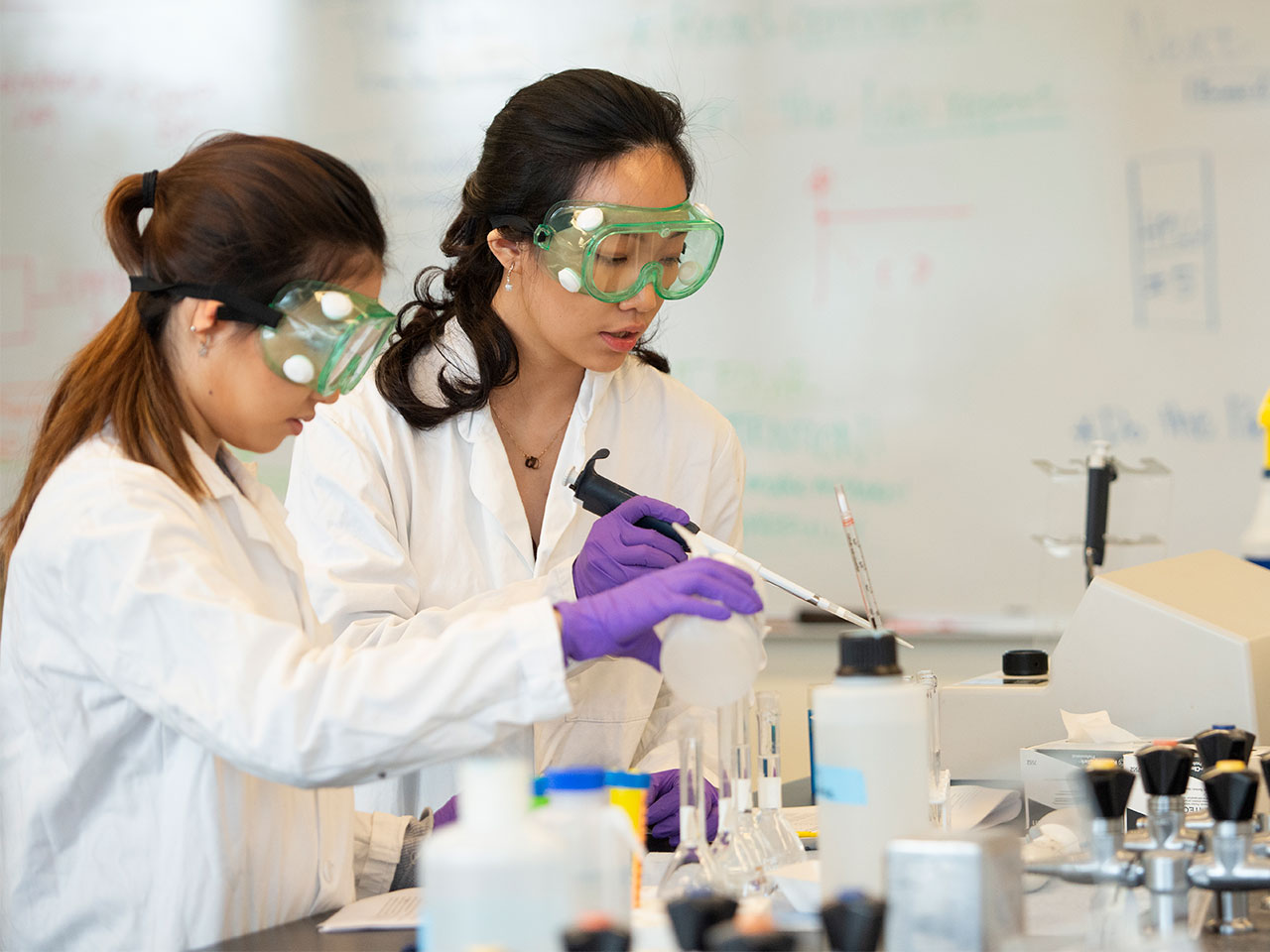 Students Melissa Lauw and Jennifer Joo in lab coats conducting a spectrophotometric measurement of teas in a UC Davis food science lab, studying the impact of phenolic compounds on flavor and health benefits.