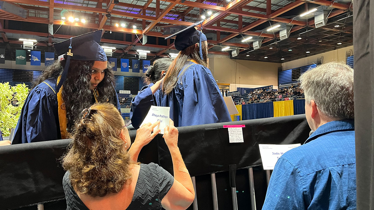 On the ramp to the graduation stage, a reader checks with a student on name pronunciation