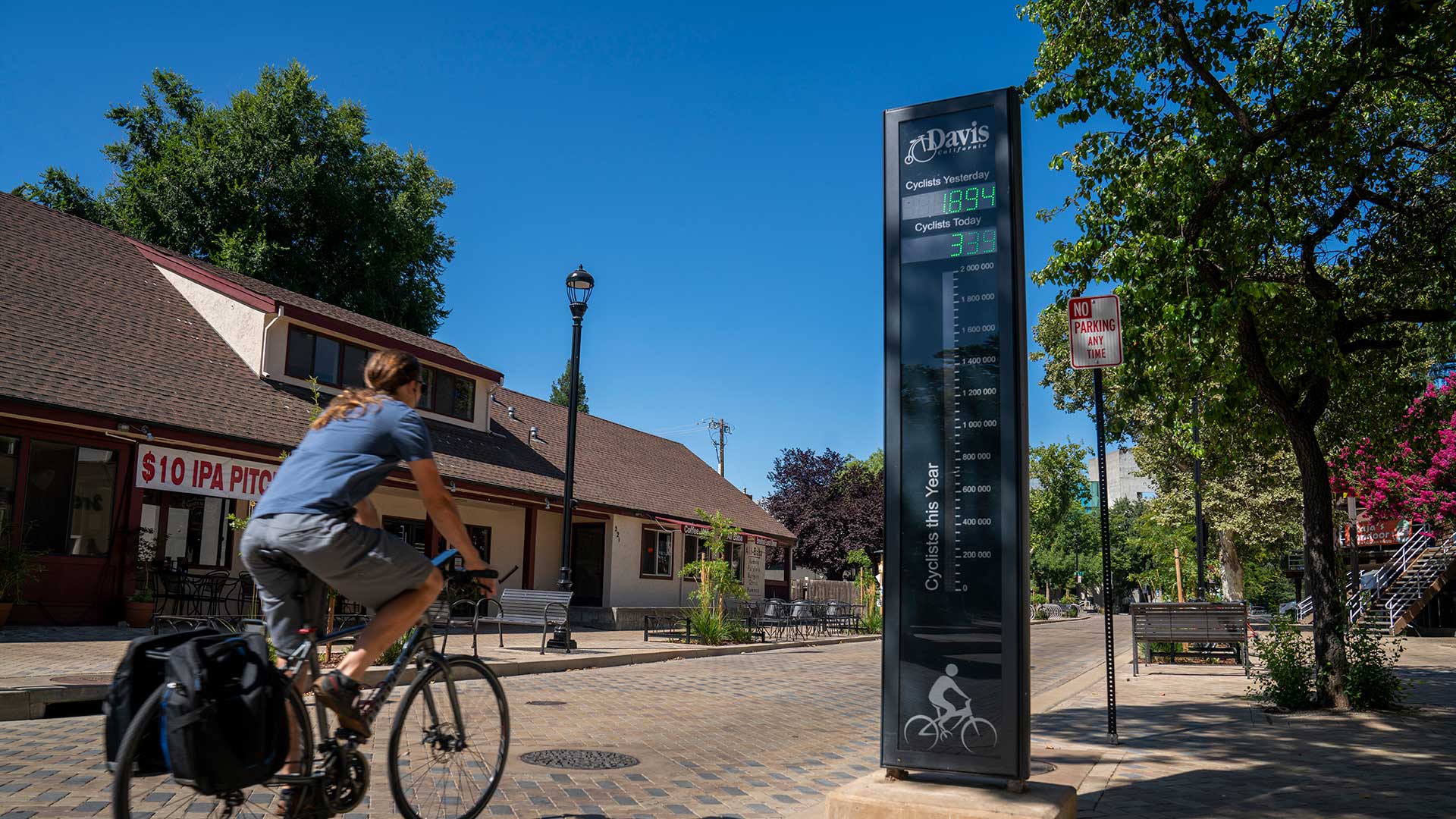 Photo of a bicyclist riding past a taller, skinny sign that displays a digital number. There is a City of Davis logo on the top of the sign.