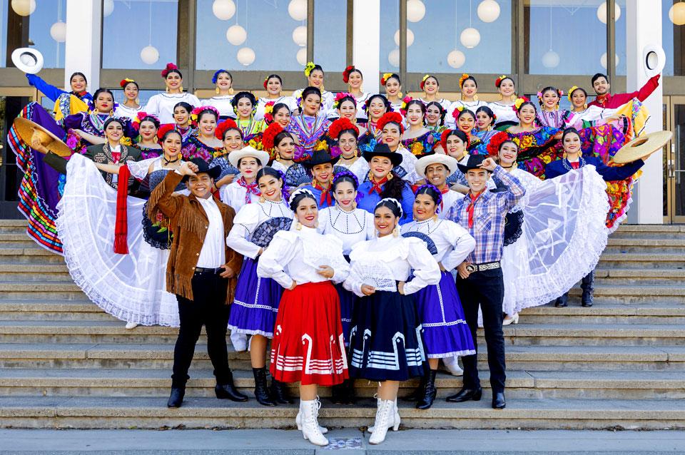 Dancers of Mexican tradition, some in colorful traditional costume, post on steps