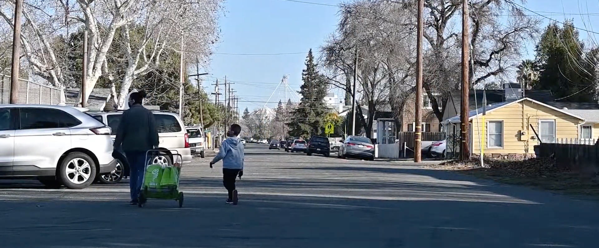 Woman and child walk down the street, with cart filled with goods from the resource table.
