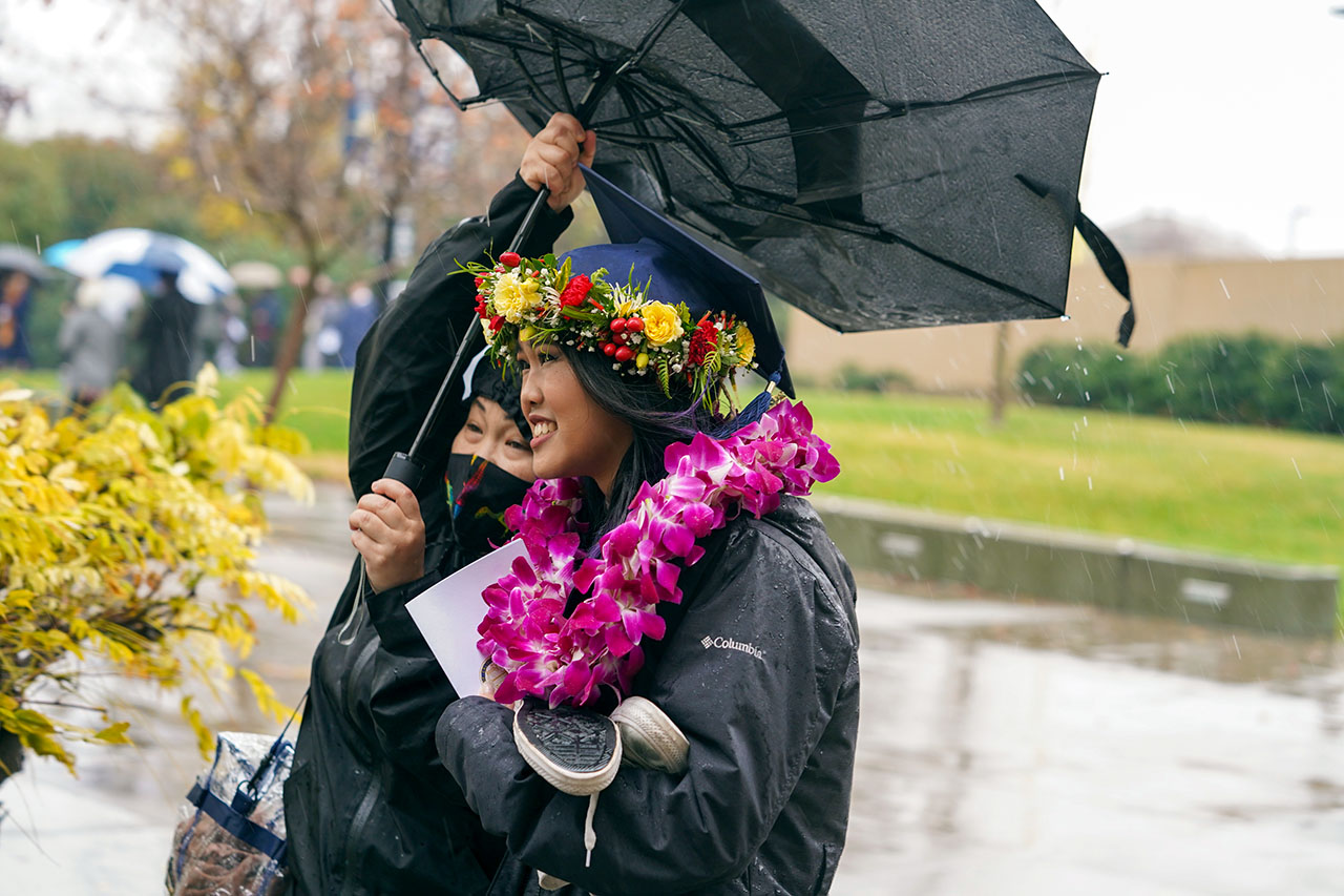 Student shelters under umbrella outside commencement ceremony