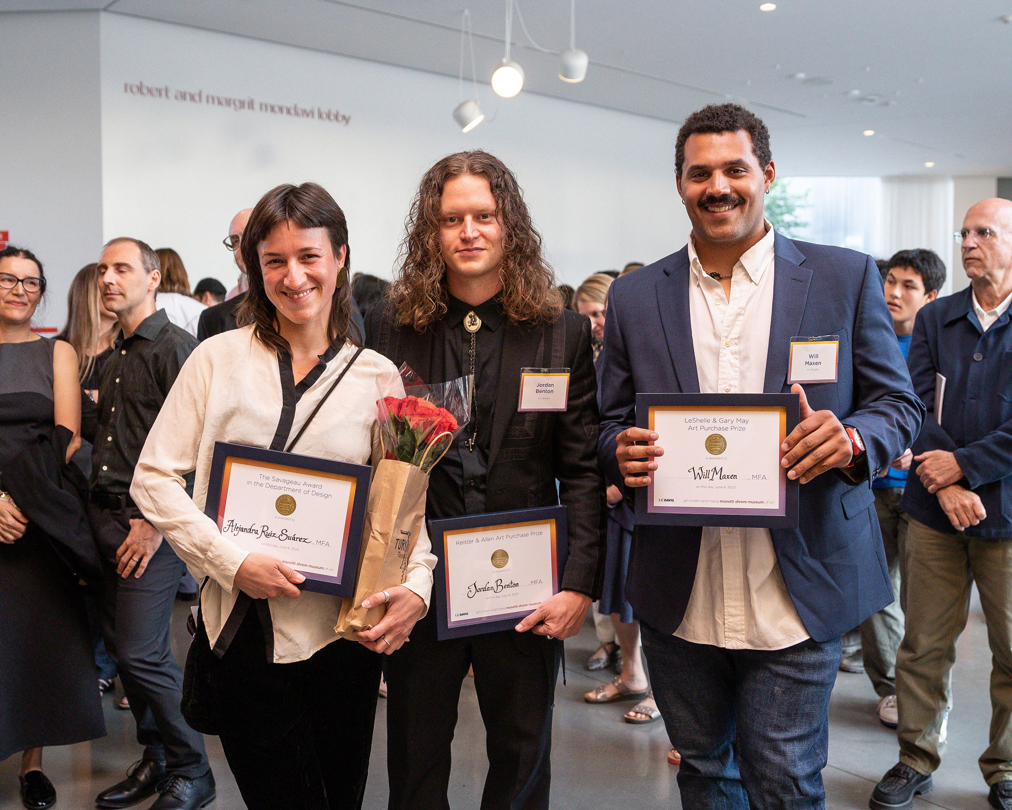 Three people holding award plaques with crowd in background in the Mondavi lobby of Manetti Shrem Museum, UC Davis