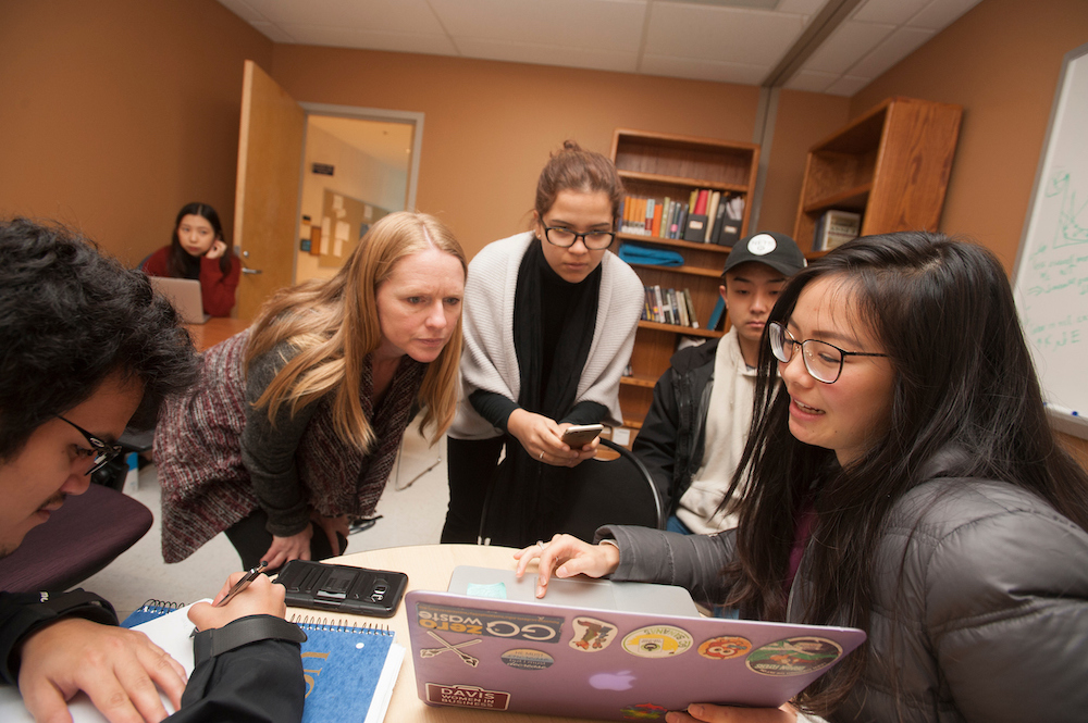 Students look at a laptop around a crowded table with their professor at UC Davis. 