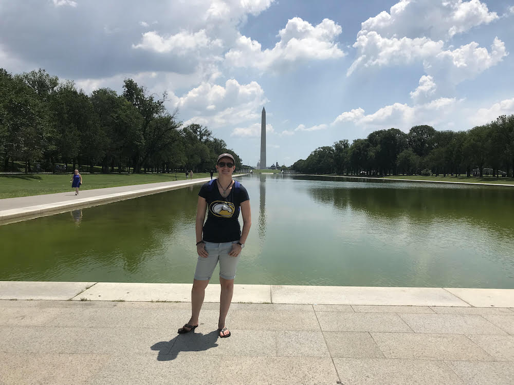 Anna stands in front of the Washington Monument in D.C. on a sunny day wearing a UC Davis T-shirt.