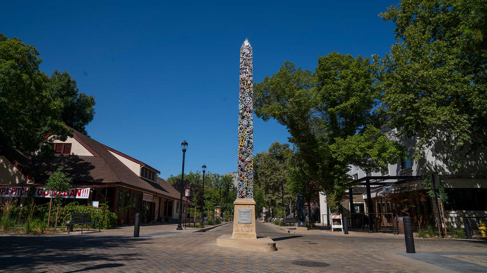 Photo of a tree lined street with an obelisk in the middle of it.