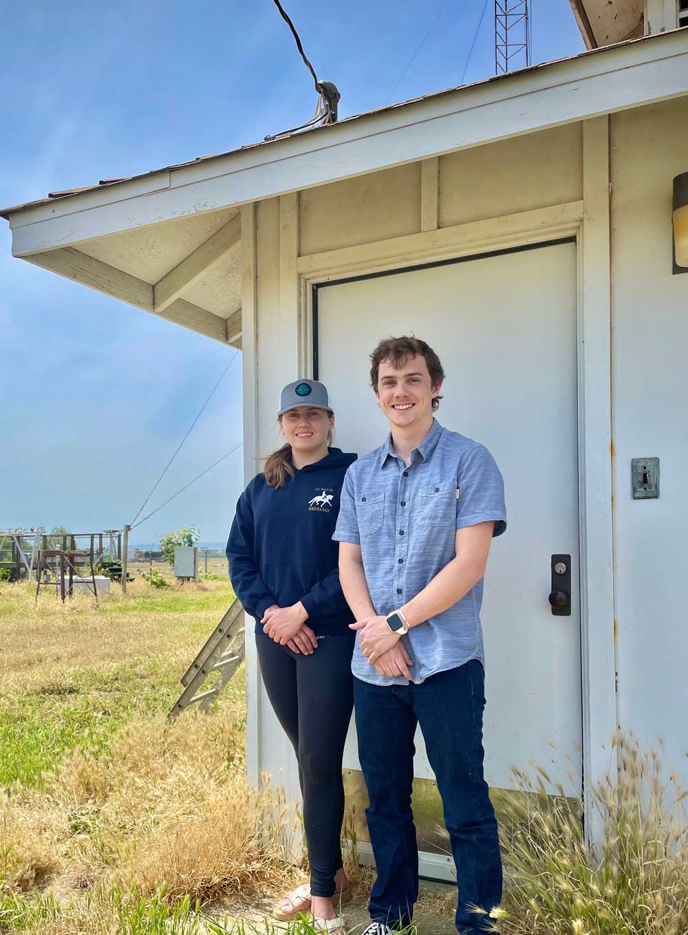 woman and man wearing blue stand in front of white shed in grassy field