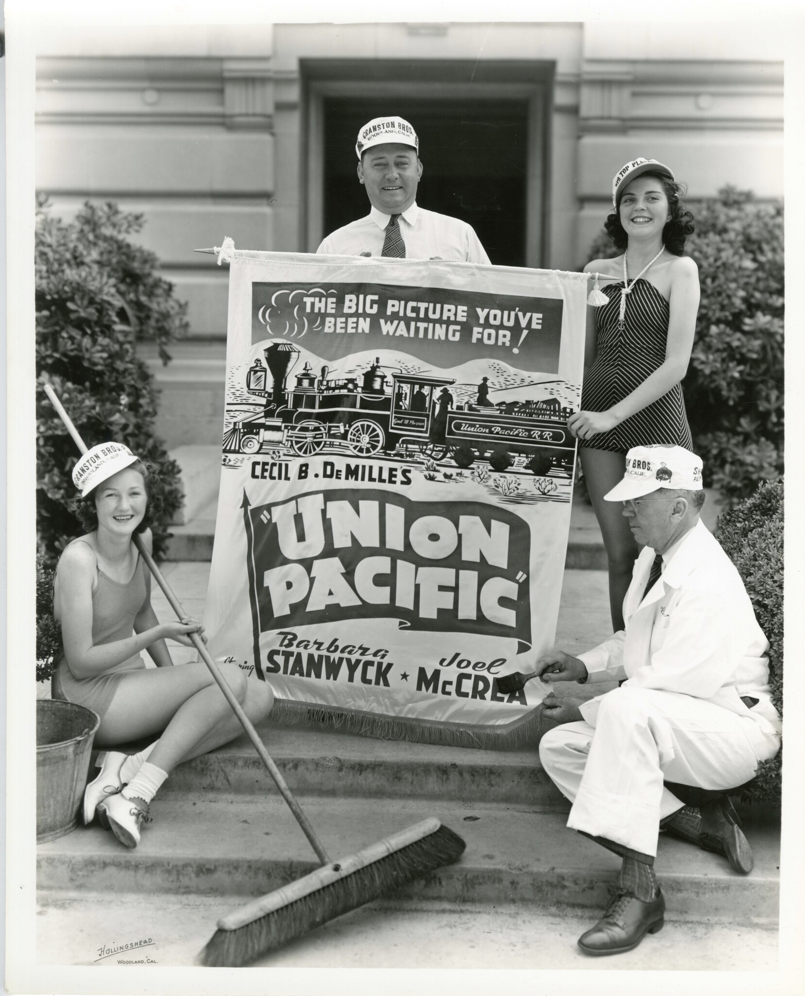 Two men and two women holding up a movie poster. One woman also holds a broom.