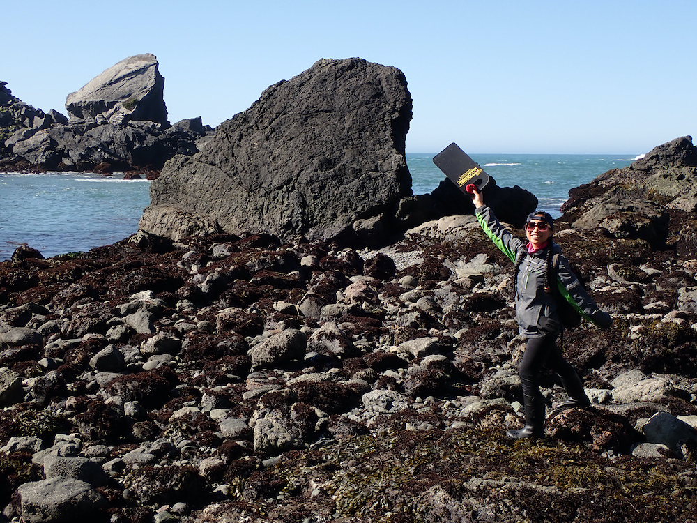 Jacquie Rajerison holds up a find at the tide pools in front of the ocean. 