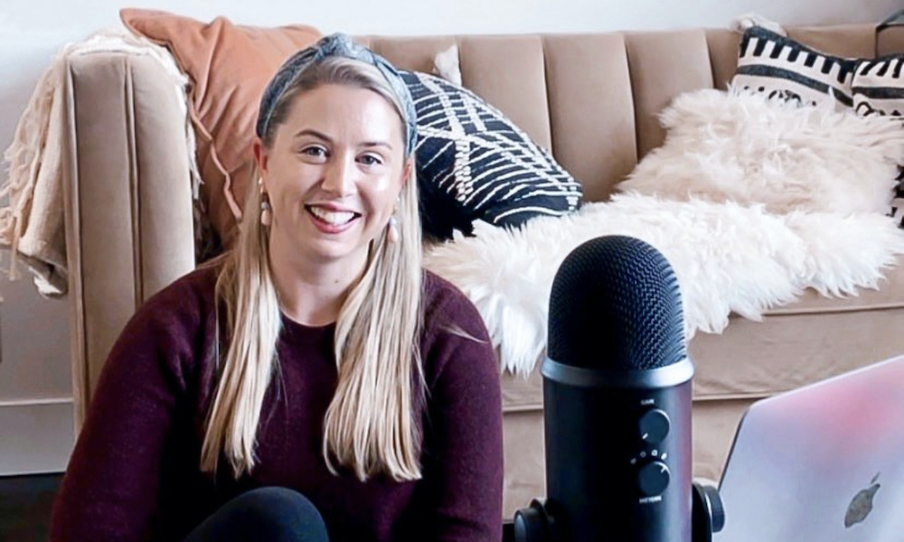Career coach Cassie smiles in her living room beside a laptop and a microphone. 