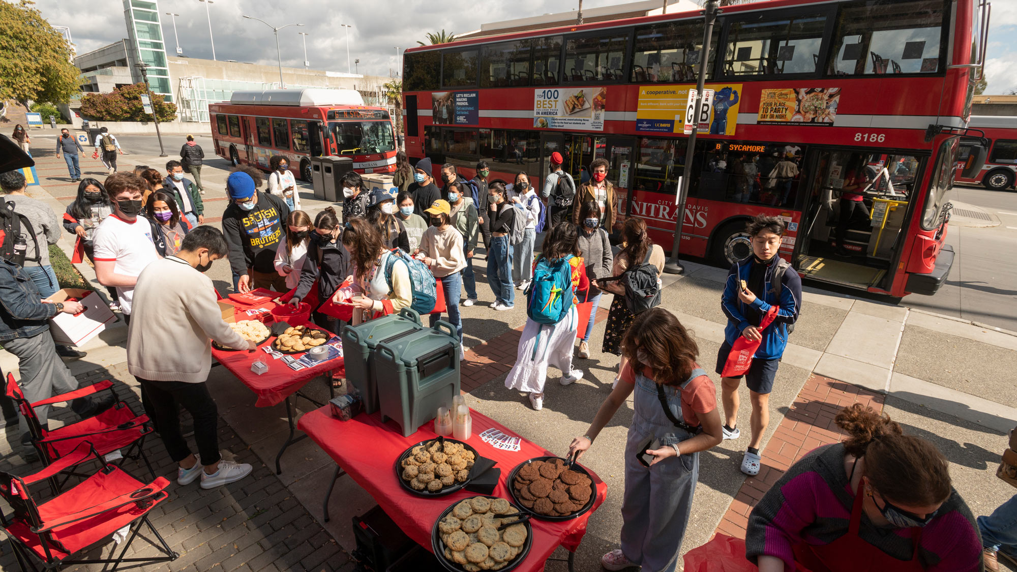 People, refreshments and swag in front of modern double-decker bus