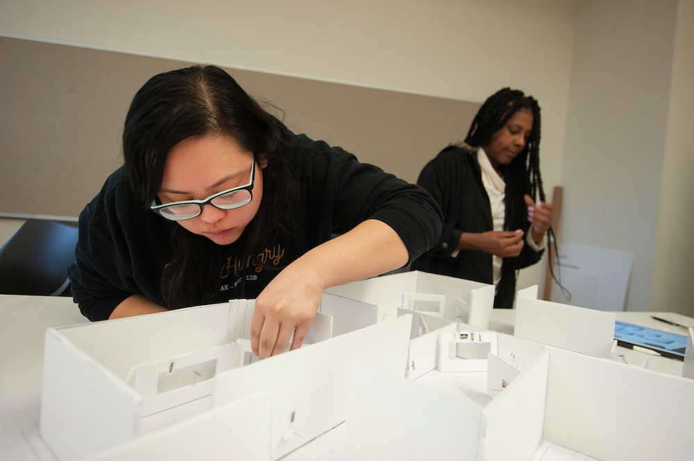 A student leans over a large white model and adjusts a room at UC Davis. 