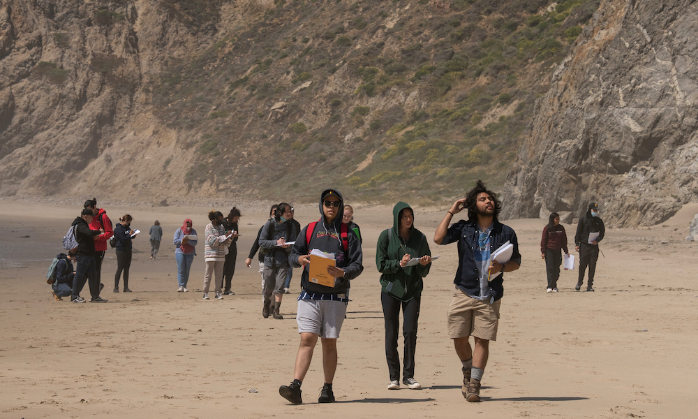 Students walk along a beach and high geological formation at UC Davis. 