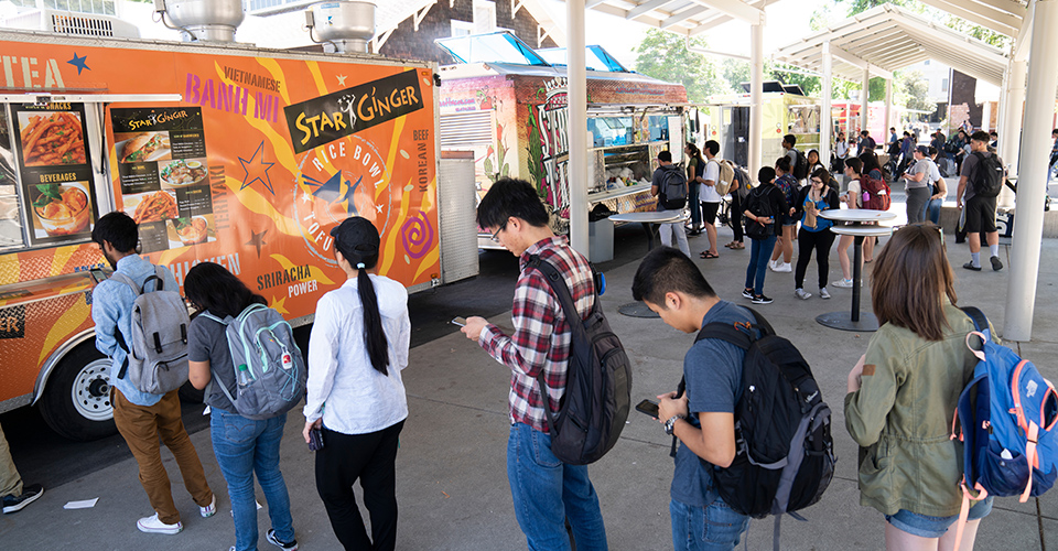 students wait for food by the food trucks parked at uc davis
