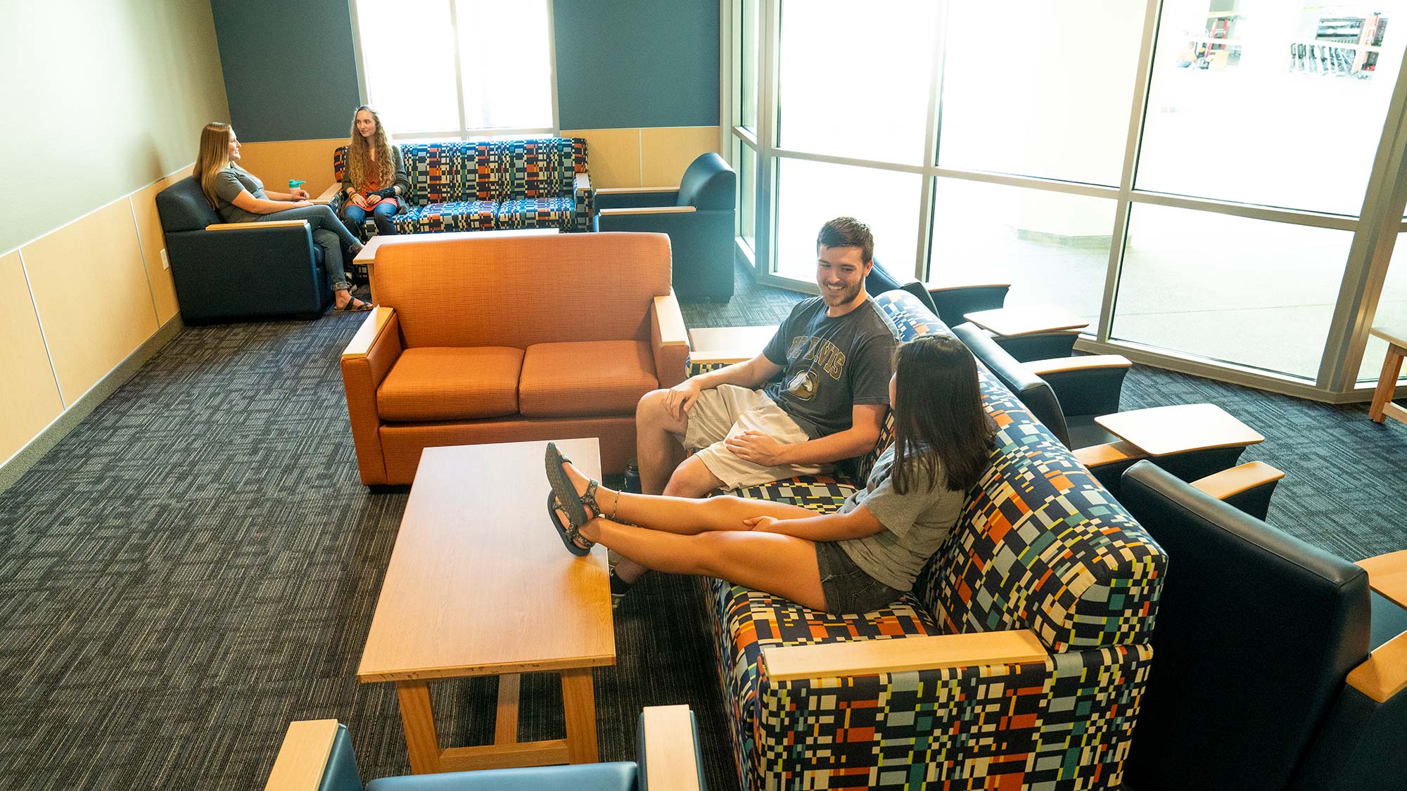 Students sit on colorful couches and talk in a newly opened lounge area of the residence hall.