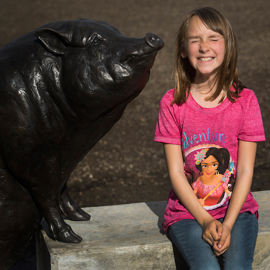A young girl sits next to a pig statue.
